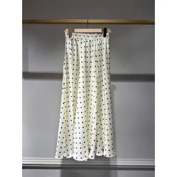 White skirt with black polka dots on a hanger against a gray background