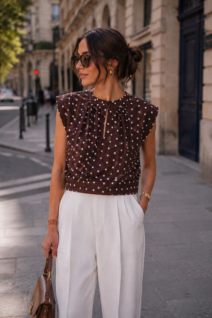 Woman in a polka dot top and white pants walking on a city street.