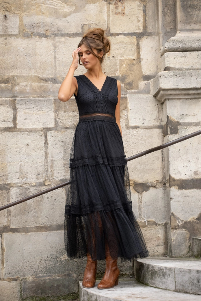 Woman wearing a black dress standing against a stone wall.