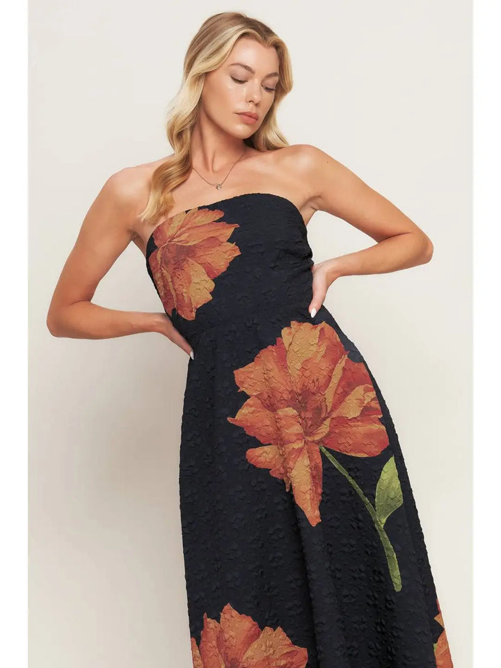 Woman wearing a black strapless dress with orange floral patterns on a plain background