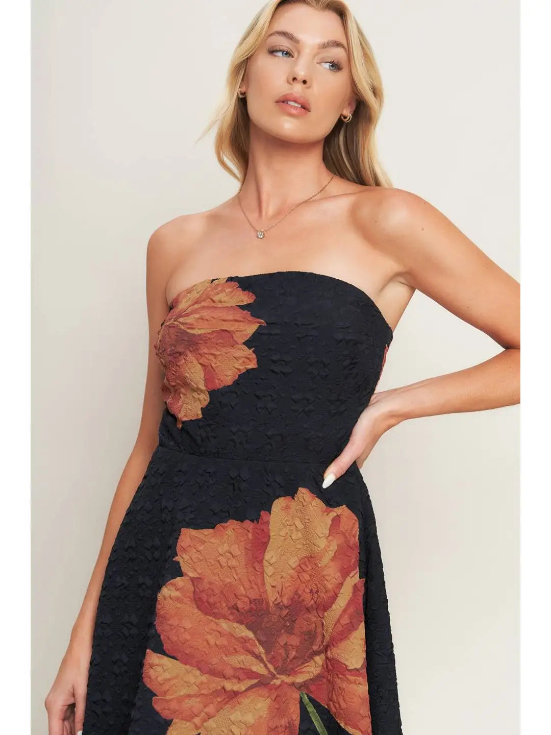 Woman wearing a black strapless dress with orange floral patterns on a plain background