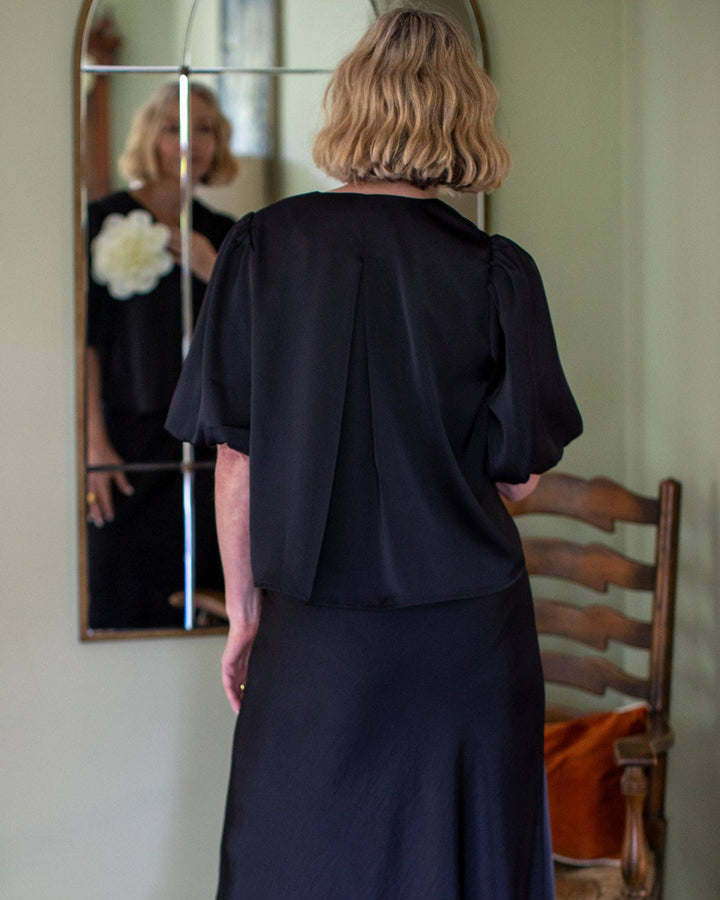 Woman wearing a black outfit standing in front of a mirror.