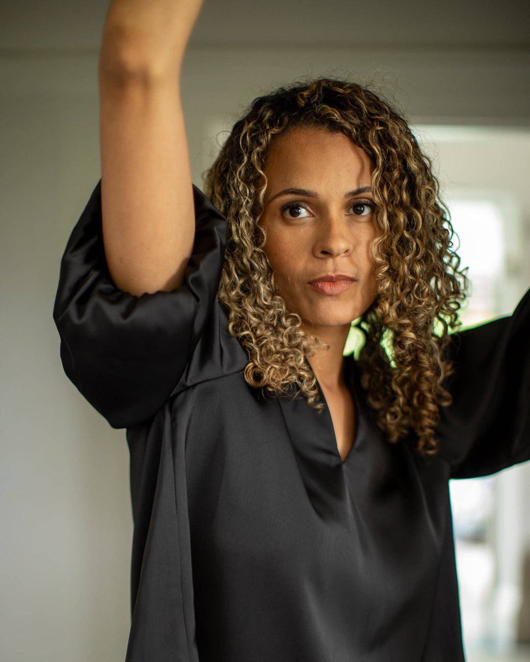 Woman in a black outfit with one arm raised, standing indoors.