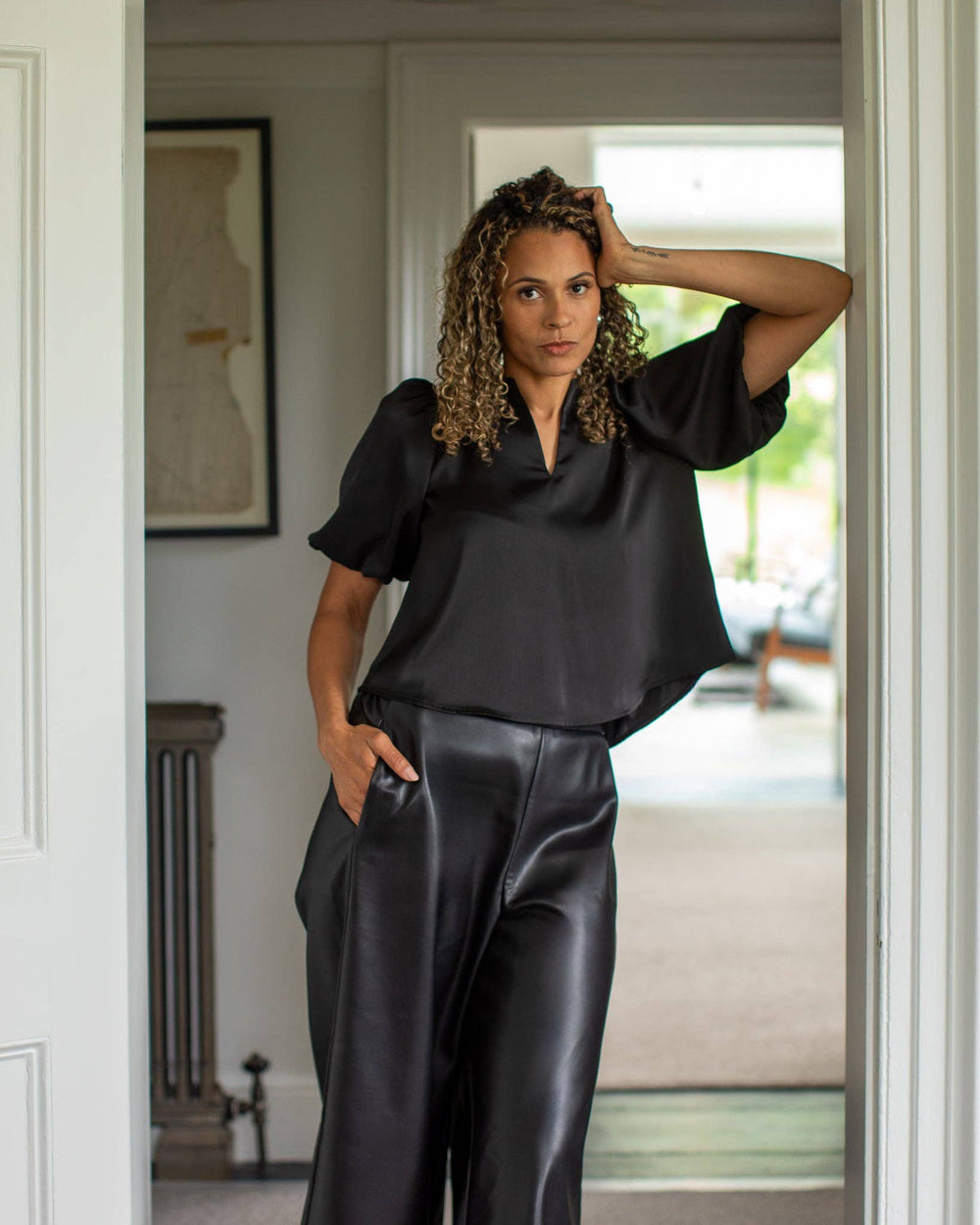Woman wearing a black satin top and pants in a room with a mirror.