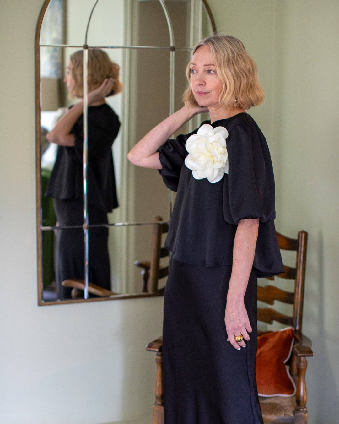Woman wearing a black dress with a white flower design, standing in front of a mirror.