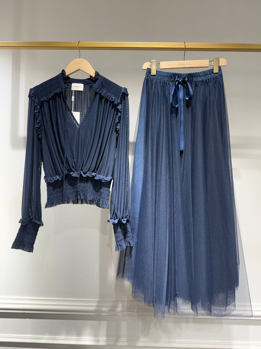 Navy blue blouse and tulle skirt on hangers against a neutral background