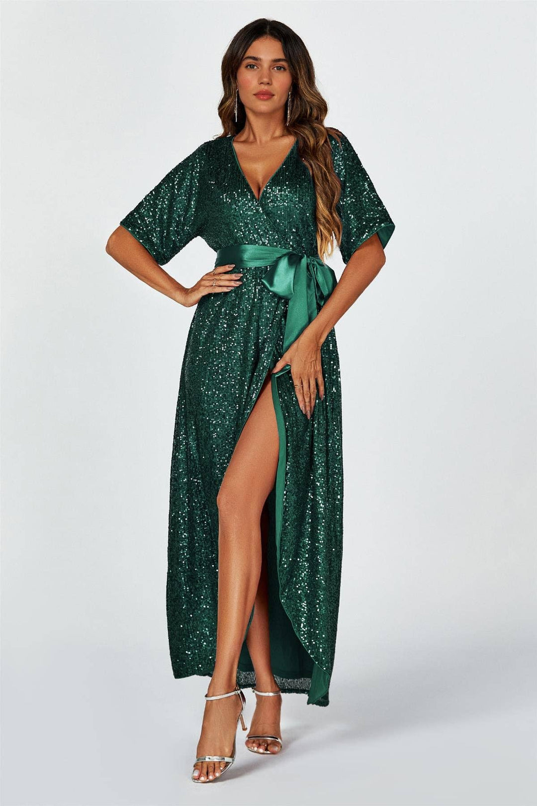 Woman wearing a green sequin dress with a slit on a white background