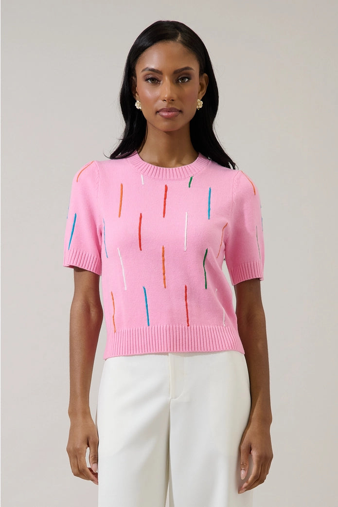 Woman wearing a pink sweater with colorful patterns against a plain background