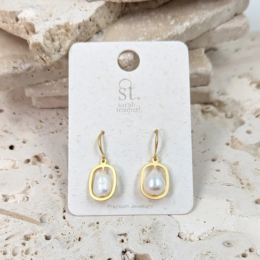 Gold earrings with pearl-like stones on a branded card against a stone background