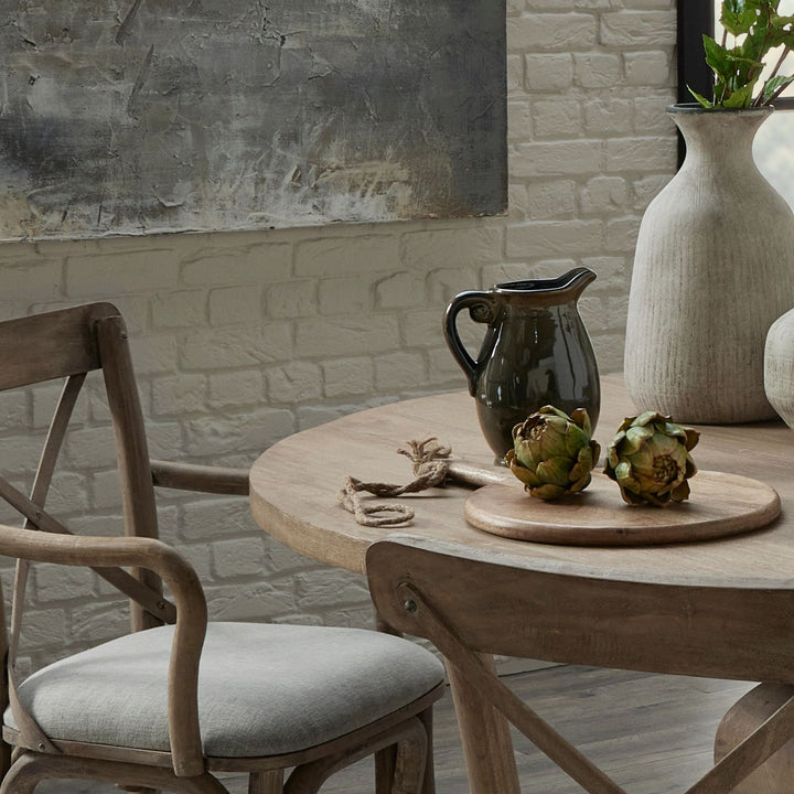 Dining area with wooden table, chairs, and decorative items against a stone wall.