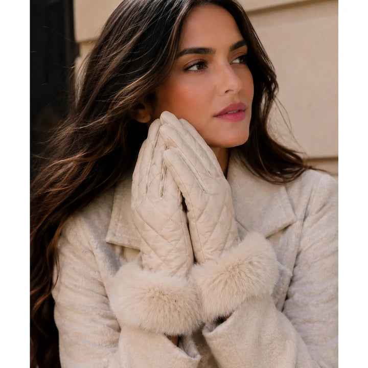 A woman wearing quilted cream gloves with fluffy faux-fur trim, posed in a close-up outdoor portrait.