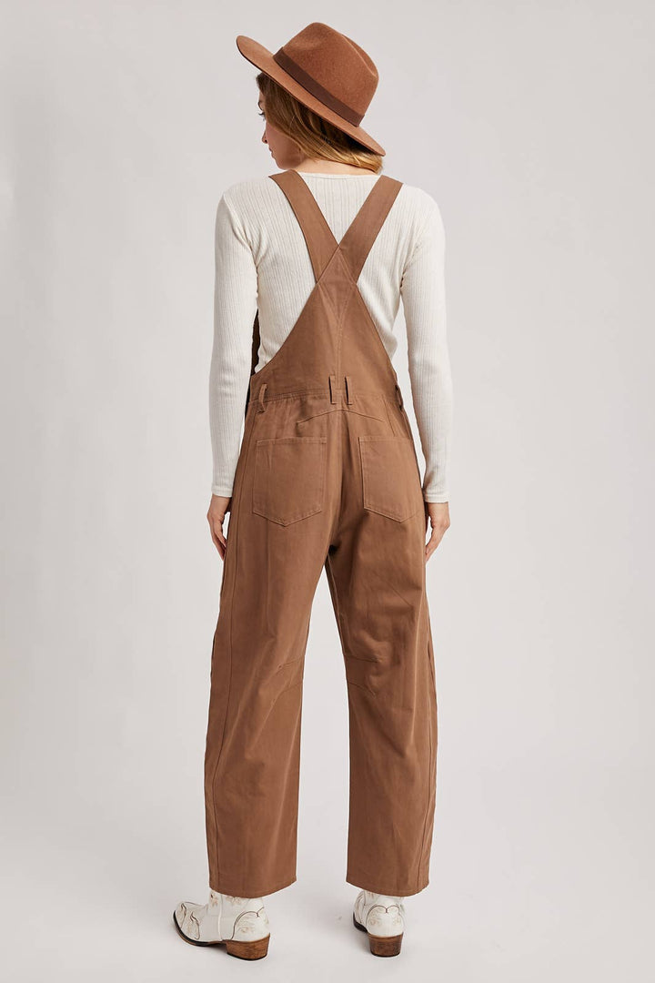 Person wearing brown overalls and a hat on a plain background