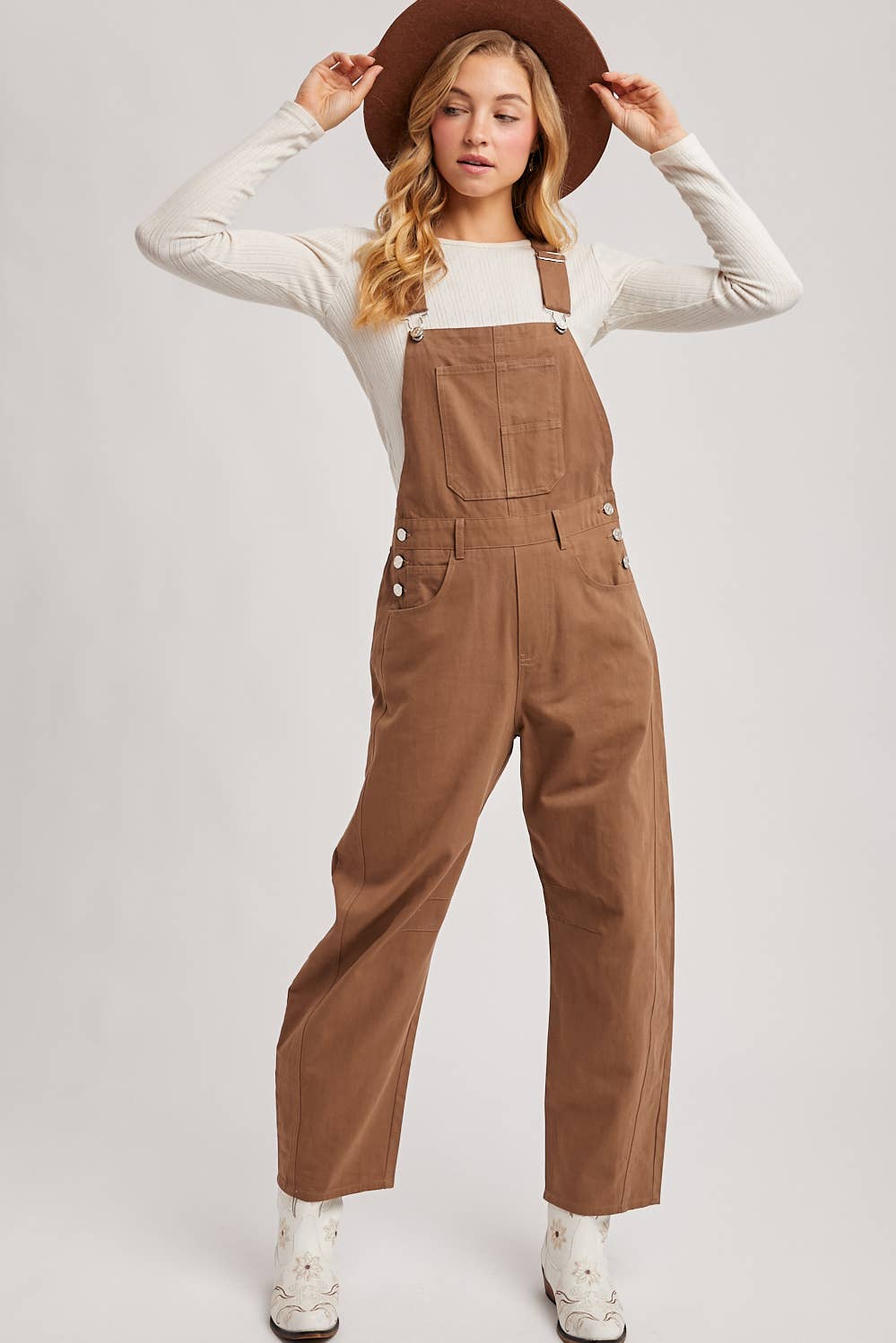 Woman wearing brown overalls and a hat on a white background