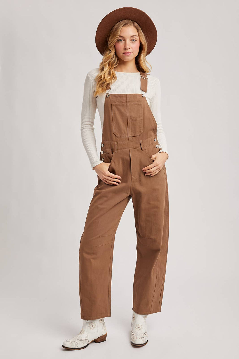 Woman wearing brown overalls and a hat on a white background