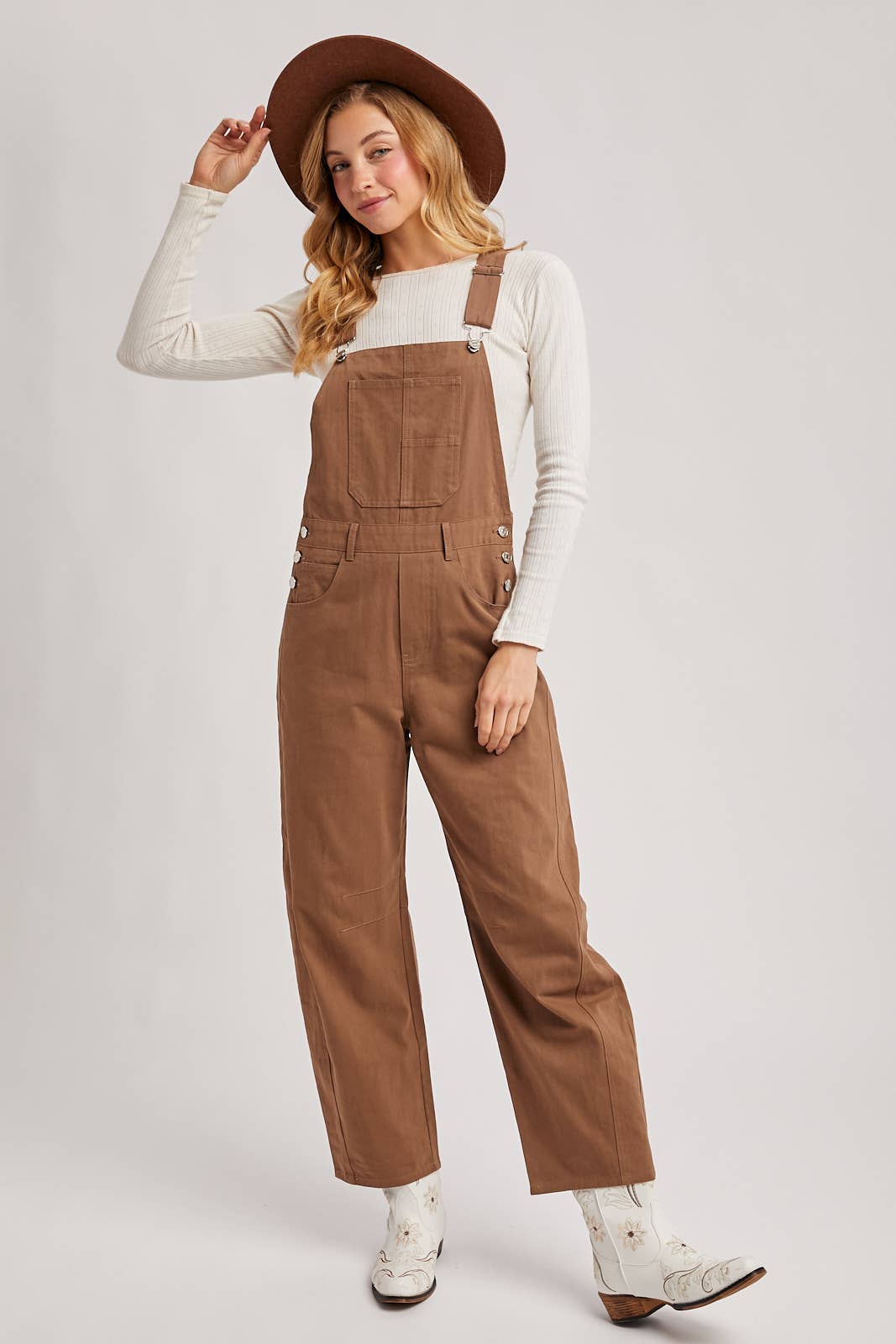 Woman wearing brown overalls and a hat on a white background