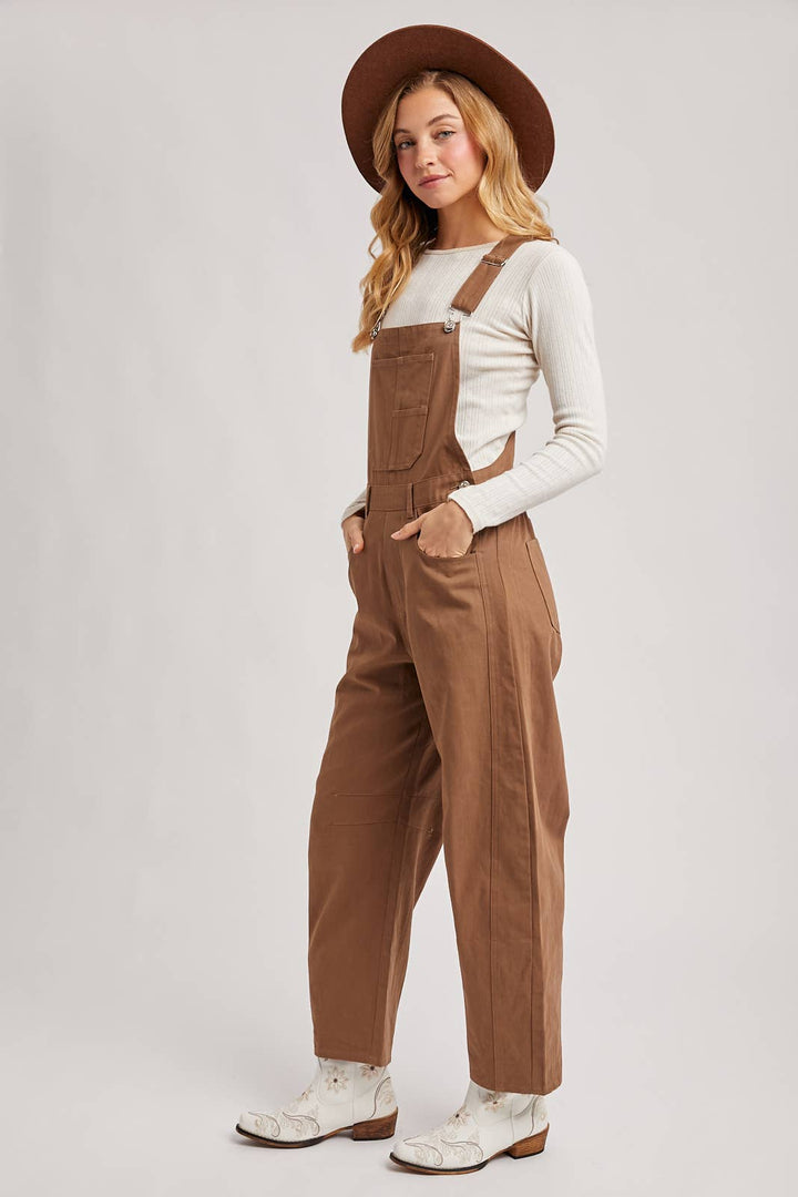 Woman wearing brown overalls and a hat on a white background