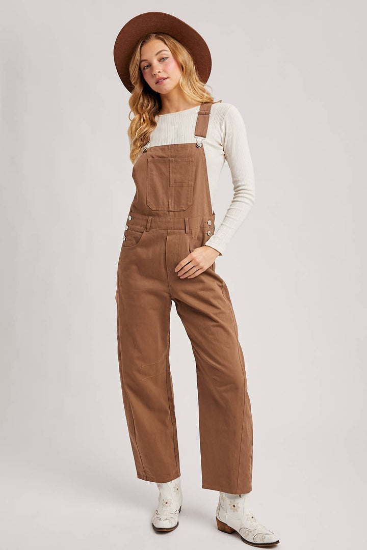 Woman wearing brown overalls and a hat on a plain background