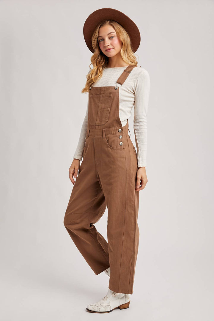 Woman wearing brown overalls and a hat on a white background