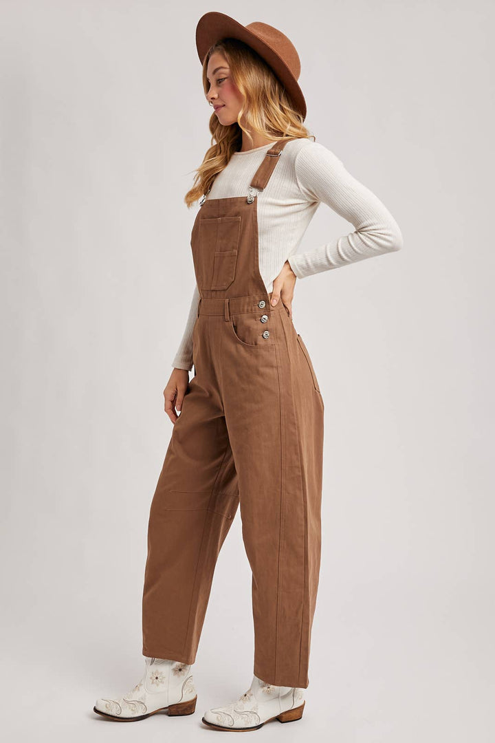 Woman wearing brown overalls and a hat on a plain background