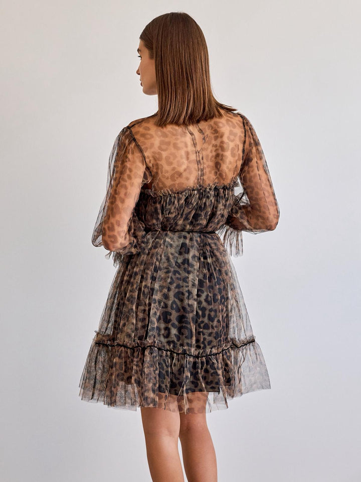 Woman wearing a leopard print dress with sheer sleeves on a plain background