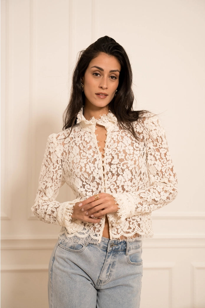 Woman wearing a white lace blouse and blue jeans against a plain background