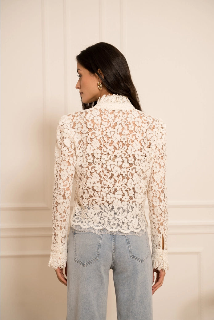 Woman wearing a lace blouse and jeans against a plain background