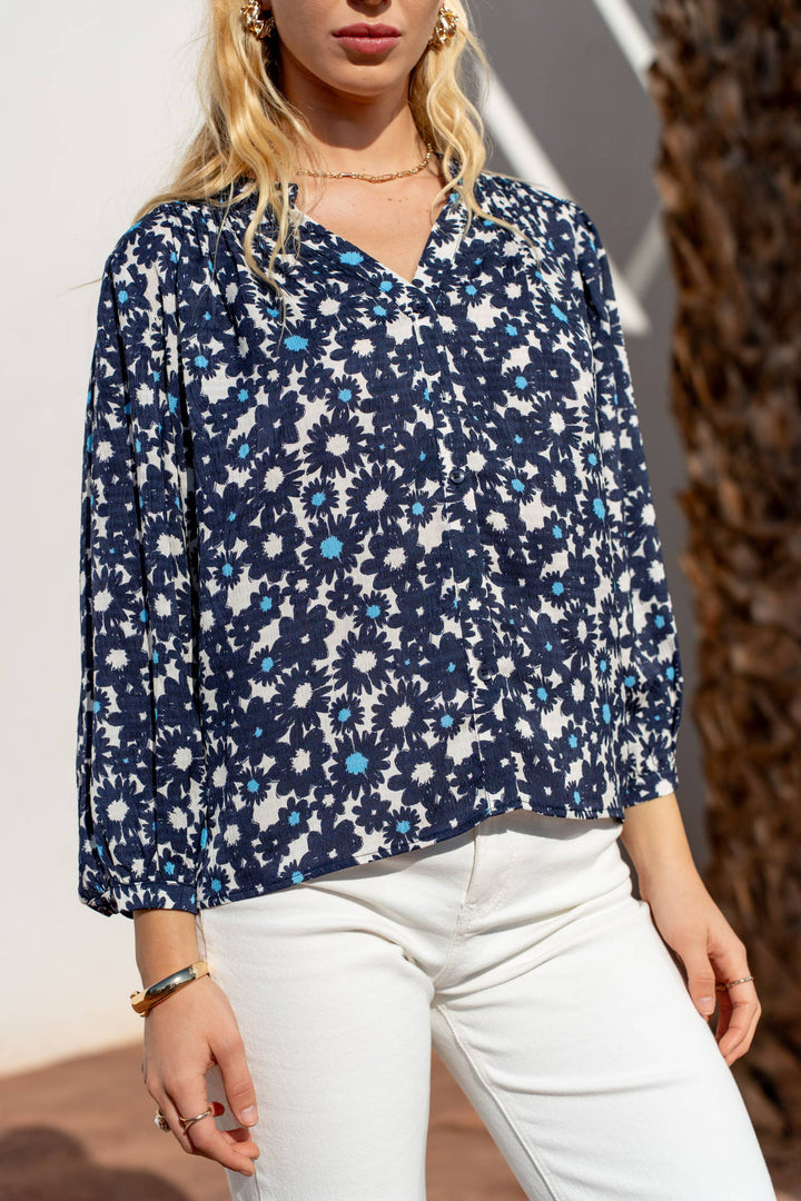 Woman wearing a blue floral blouse and white pants outdoors.