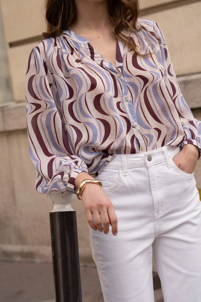 Person wearing a patterned blouse and white pants with a blurred background