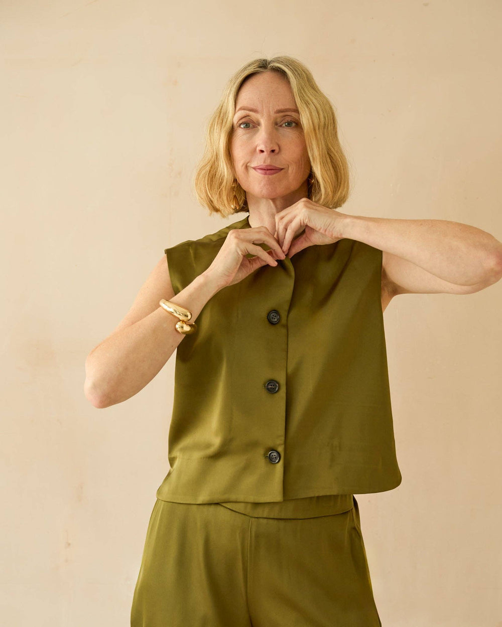 Woman wearing a green sleeveless top and pants against a beige background