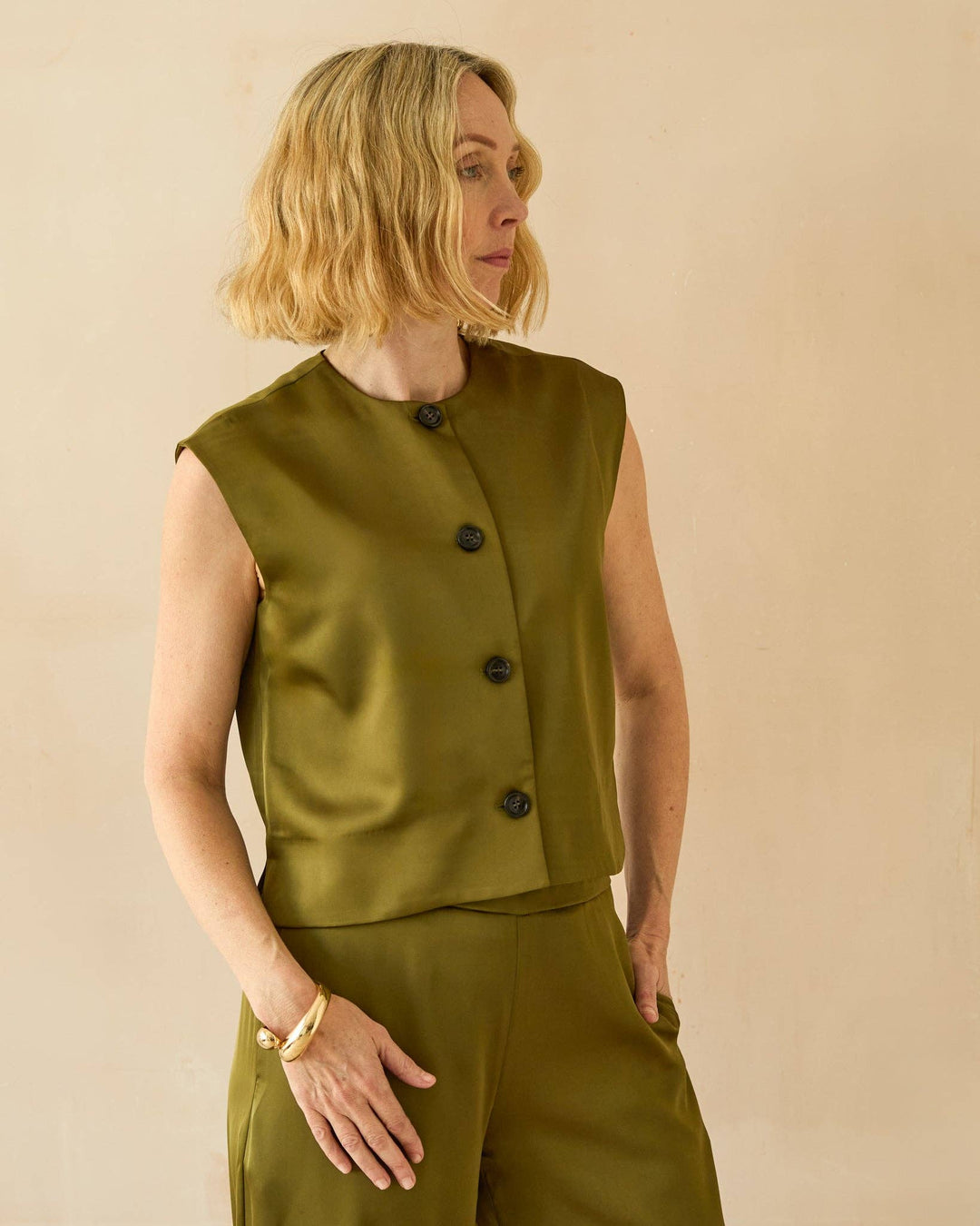 Woman wearing a green vest and pants against a beige background
