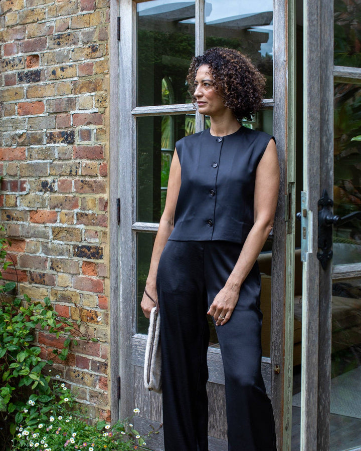 Woman in a black outfit standing in front of a brick wall and open door.