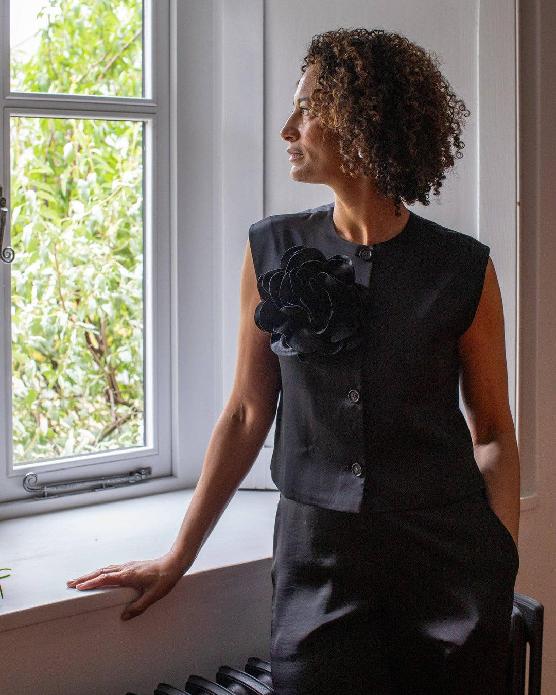 Woman in a black dress with floral details sitting by a window