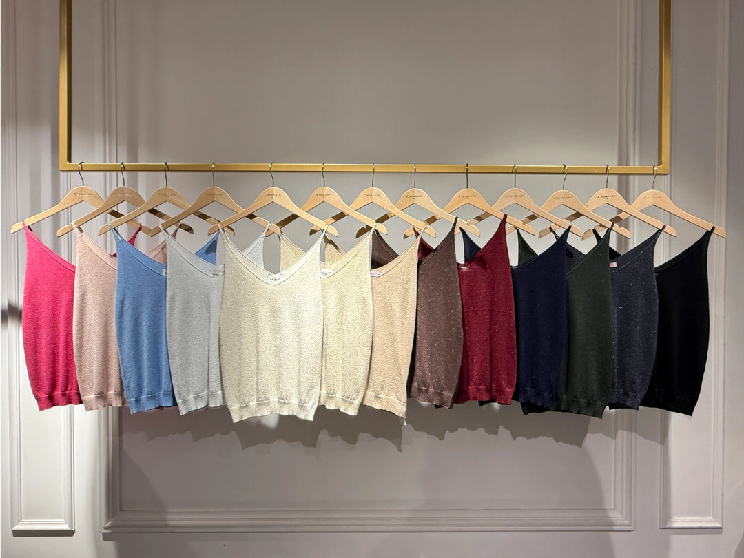 Row of colorful tank tops hanging on a rack against a neutral wall.