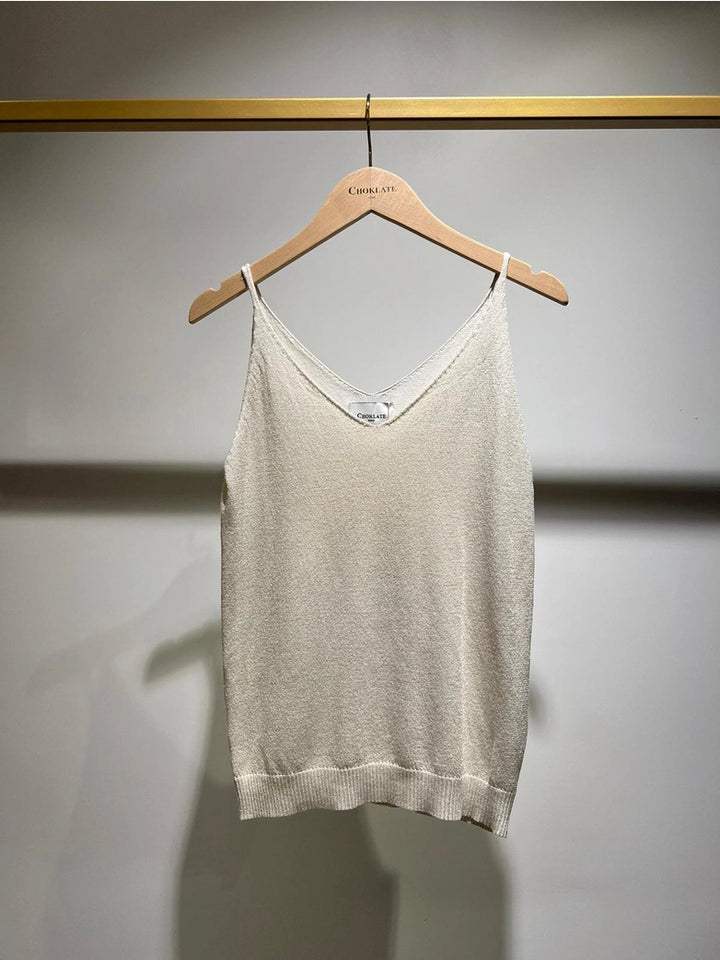 Beige tank top hanging on a wooden hanger against a gray wall.