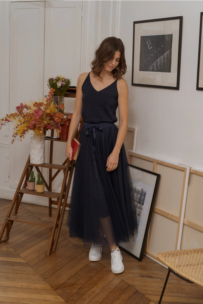 Woman in a black dress standing in a room with wooden floor and framed pictures on the wall.