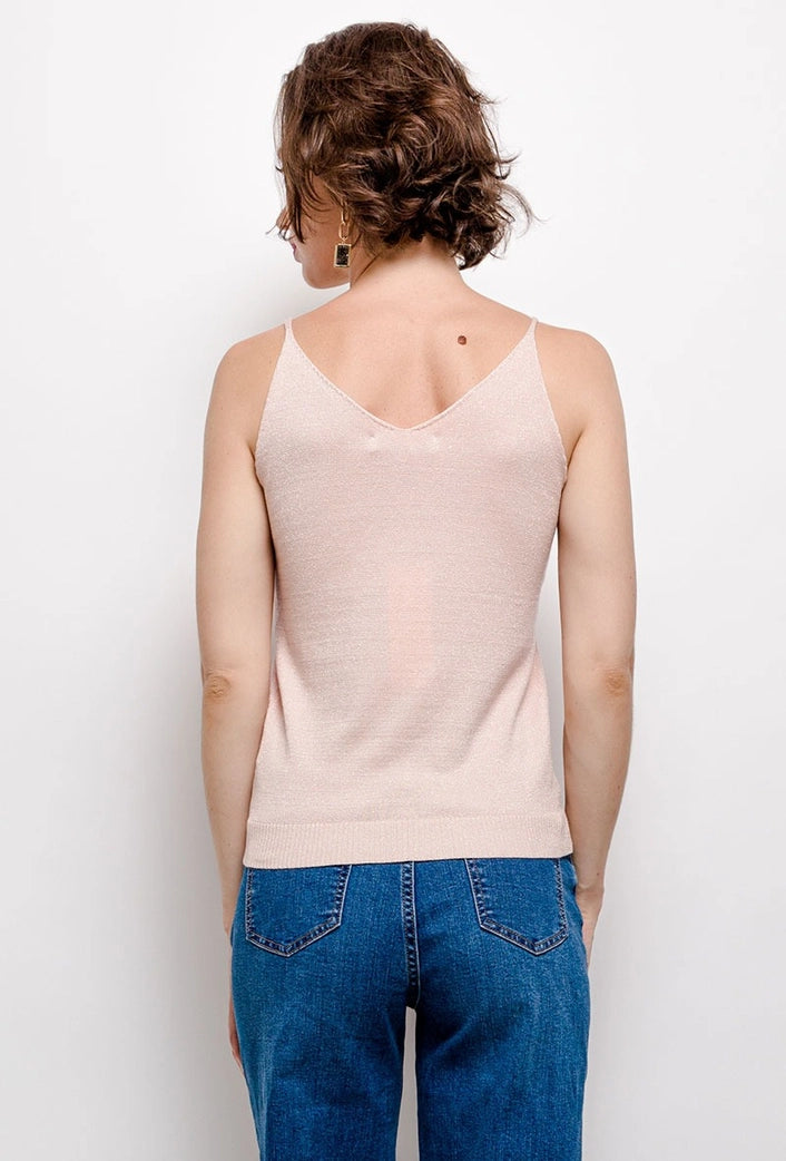 Person wearing a beige tank top and blue jeans against a white background