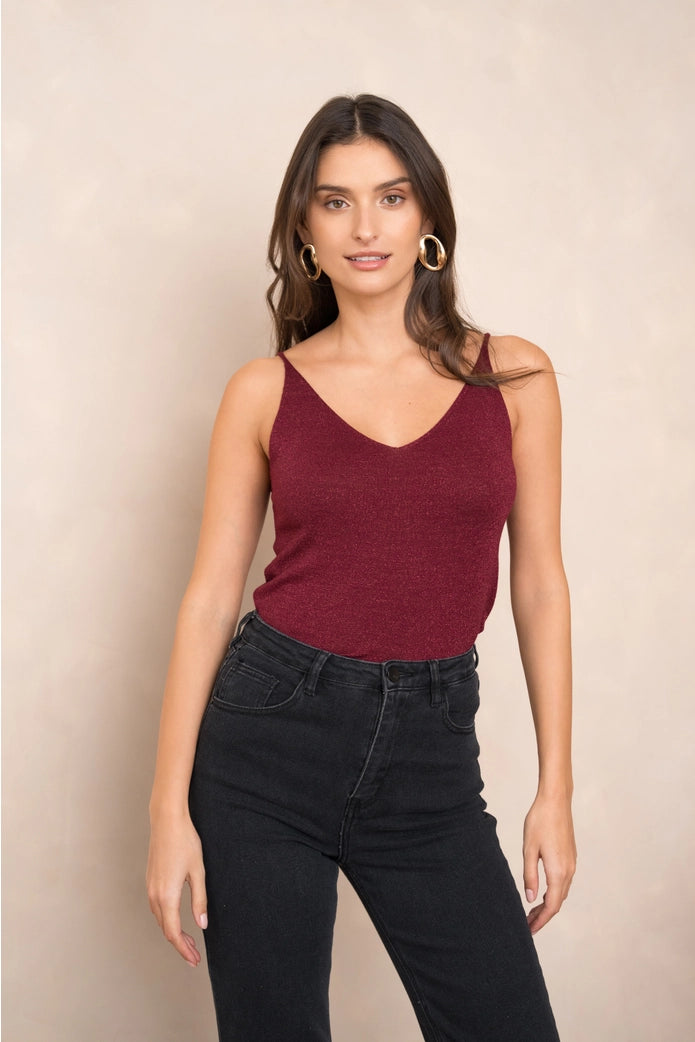 Woman wearing a burgundy tank top and black jeans against a beige background