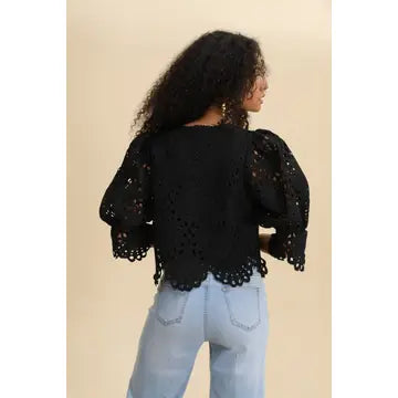 Woman wearing a black lace top and light blue jeans against a beige background