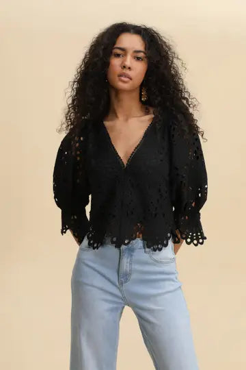 Woman wearing a black lace top and light blue jeans against a beige background