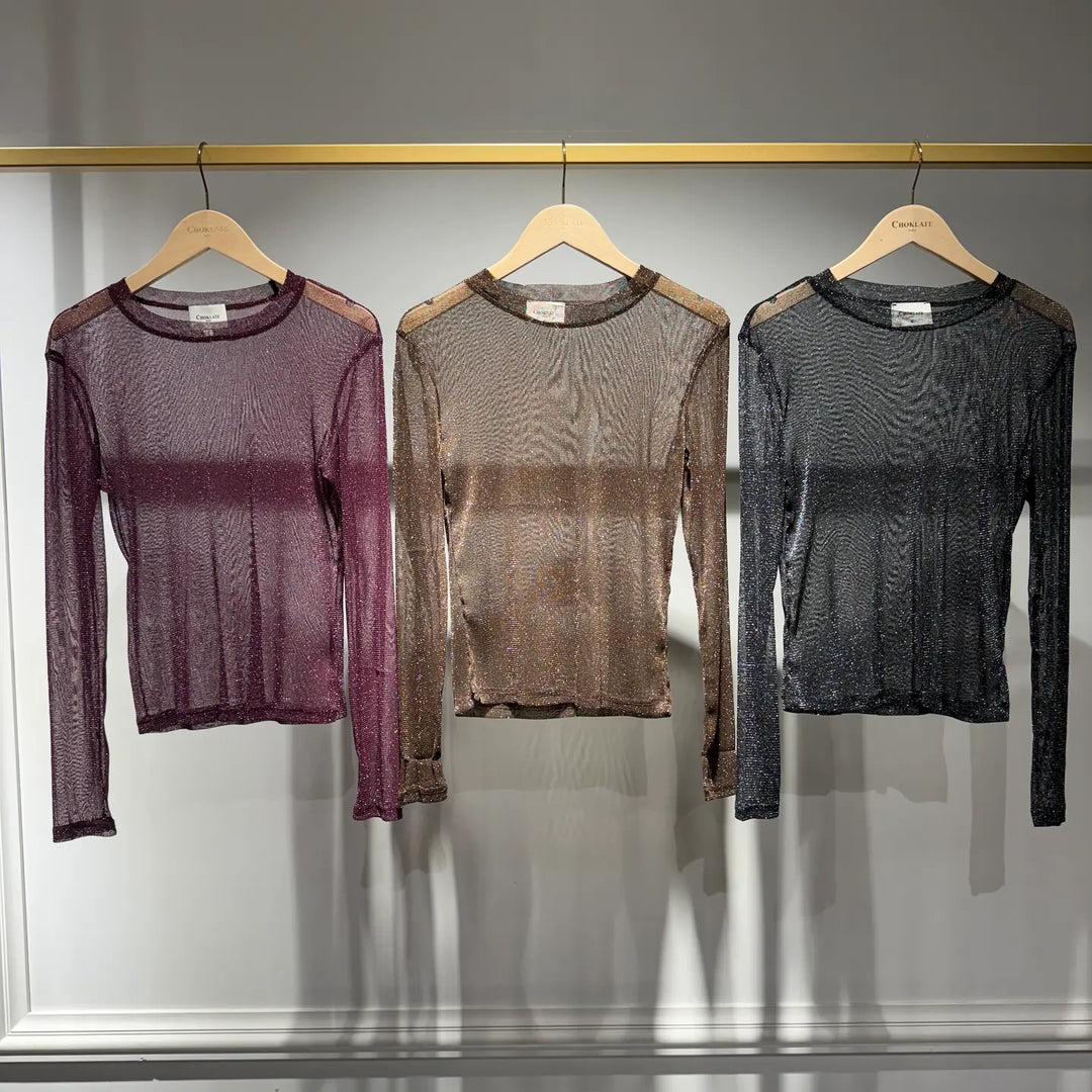 Three sheer long-sleeve shirts in purple, brown, and black hanging on a rack.