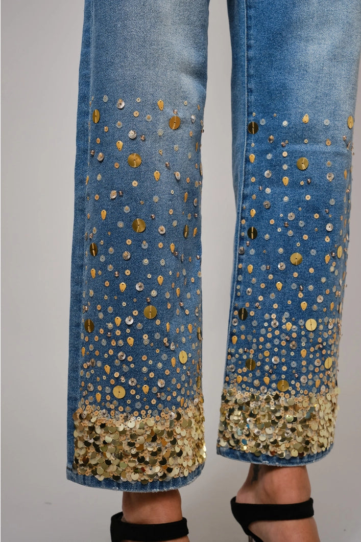 Blue jeans with gold sequin embellishments on a plain background