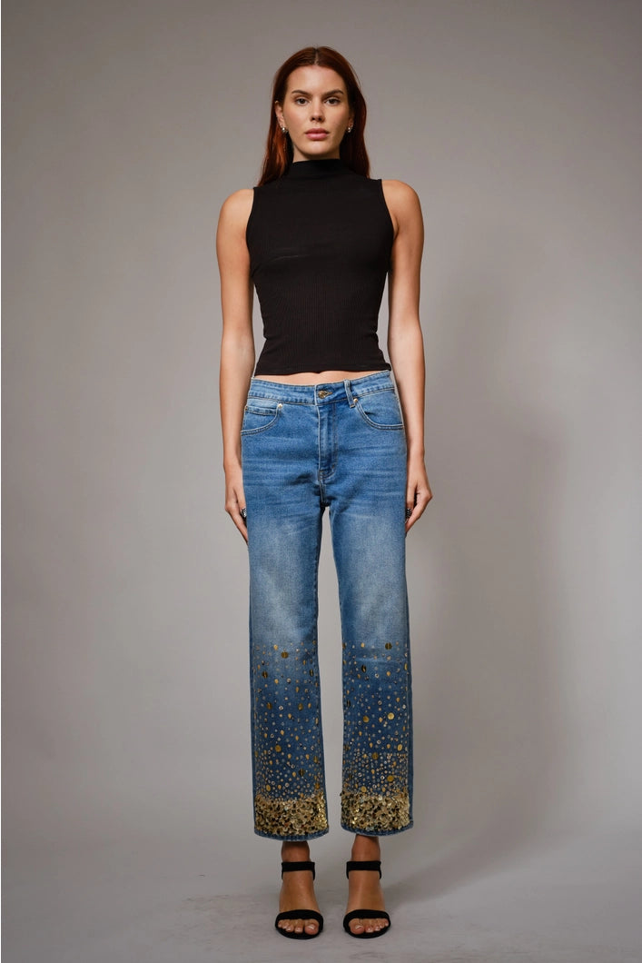 Woman wearing a black sleeveless top and blue jeans with gold accents on a gray background