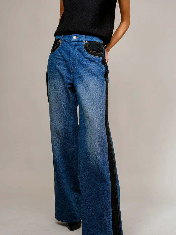 Blue jeans with black accents worn by a person on a neutral background