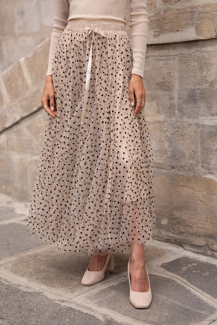 Person wearing a long, light-colored skirt with a subtle pattern against a stone wall.