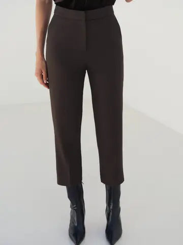 A model wearing high-waisted, straight-leg cropped trousers in a dark brown color, paired with black pointed-toe ankle boots against a clean white studio background.
