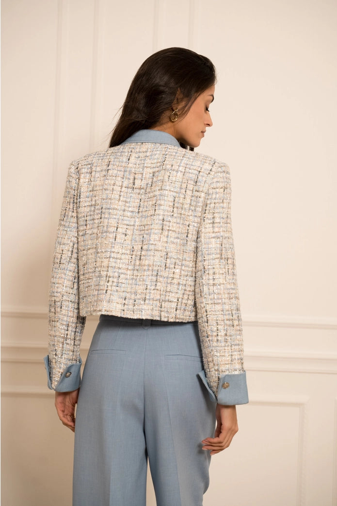 Woman wearing a patterned jacket and light blue pants against a neutral background