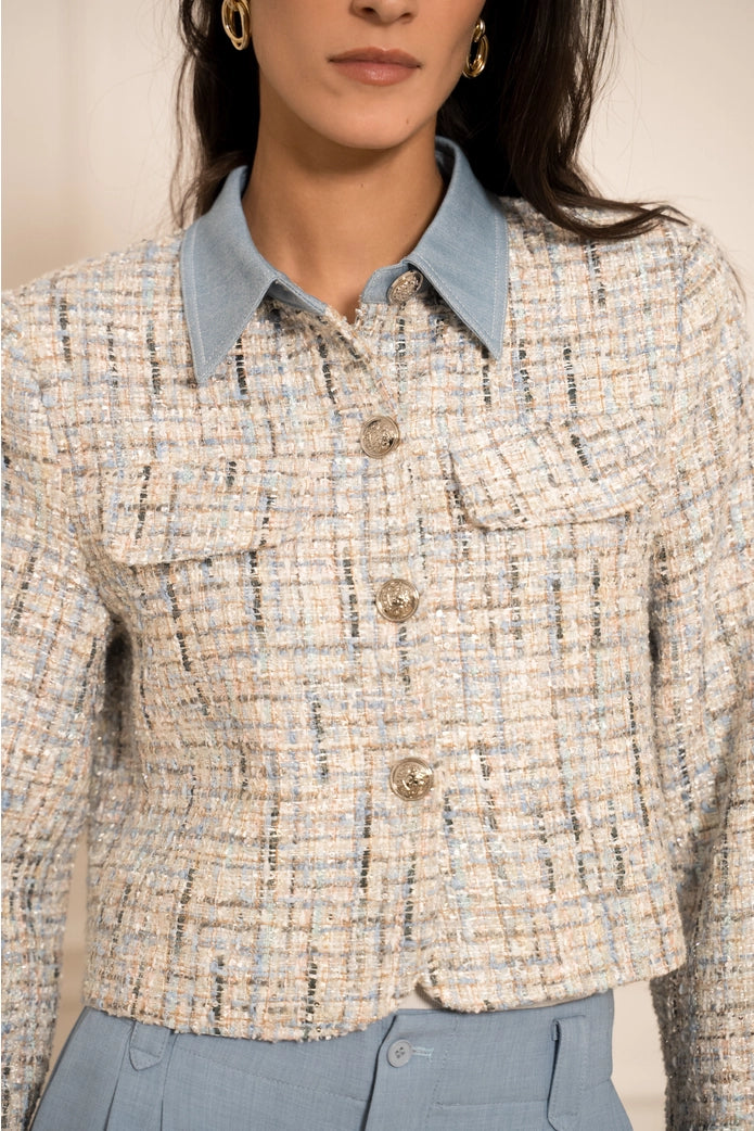 Woman wearing a tweed jacket with a blue shirt underneath, on a plain background