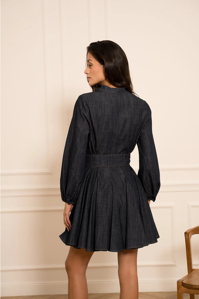 Woman wearing a black denim dress against a beige wall.
