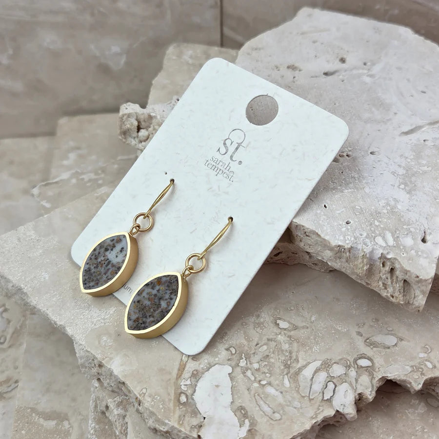 Gold earrings with druzy stones on a branded card, placed on textured stone surface