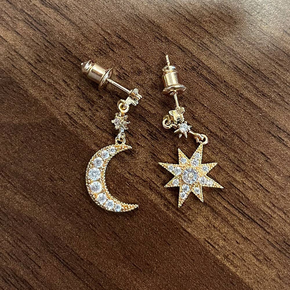 Pair of gold earrings with moon and star designs on a wooden surface